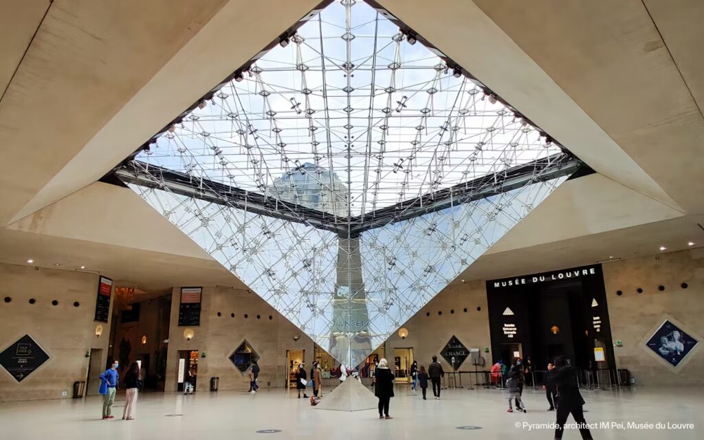 Louvre Museum pyramid interior view, Paris. "Musée du Louvre" text is visible.